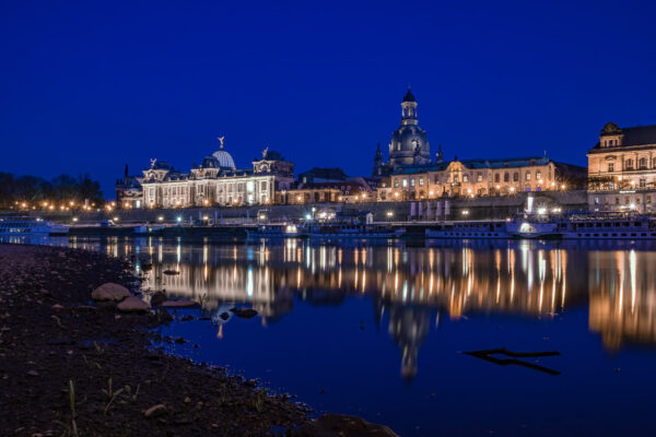 Vom Königsufer aus direkt an der Elbe und noch während der Blauen Stunde ist das altstädter Elbufer mit der Brühl'schen Terrasse Dresdens zu sehen. Etwas versteckt ist die zitronenpressenartige Kuppel der Kunstakademie und um so präsenter die Kuppel der Frauenkirche sichtbar. Sämtliche Lichtquellen spiegeln sich in der Wasseroberfläche der Elbe. Die Dampfer der Weißen Flotte liegen an ihren Anlegestellen.