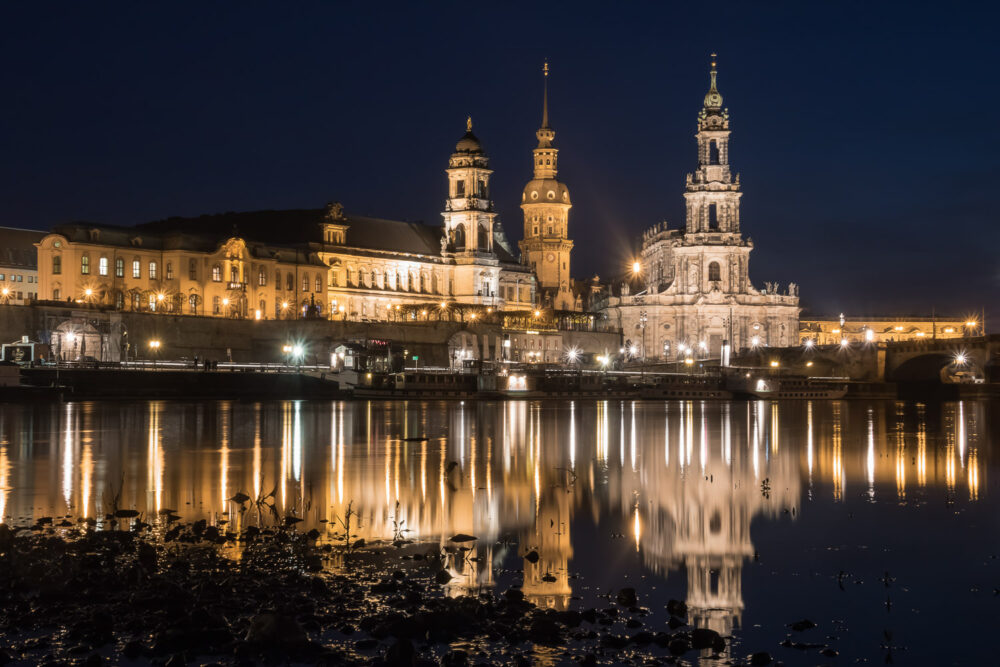 Vom Königsufer aus direkt an der Elbe sind die drei Türme des Ständehauses, des Schlosses Dresden – der "Hausmannsturm" – und der katholischen Hofkirche zu sehen. Unterhalb dessen verläuft das altstädter Elbufer mit der Brühl'schen Terrasse. Sämtliche Lichtquellen spiegeln sich in der Wasseroberfläche der Elbe. Die Dampfer der Weißen Flotte liegen an ihren Anlegestellen. Entstanden beim Fotoworkshop Blaue Stunde & Nachtfotografie.