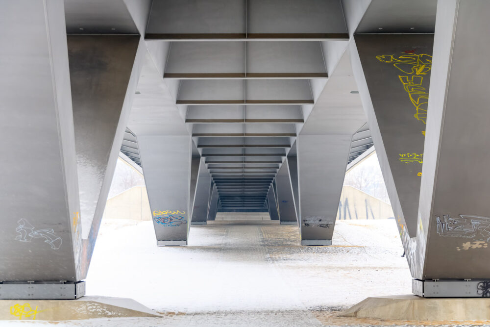 Das Stahlgerüst unterhalb der Dresdner Waldschlösschenbrücke symetrisch fotografiert und mit einigen Grafitis dekoriert erzeugt sehr viele geometrische Figuren und interessante Linien im Bild. In den letzten Tagen hat es sehr viel geschneit. Selbst unter der Brücke und auf einigen Stahlträgern liegt eine zarte Schneedecke.